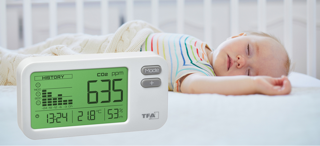 Baby sleeping in a crib with a CO2 monitor displaying 635 ppm.