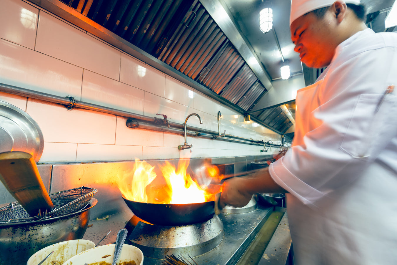 Chef cooking over a flaming wok in a professional kitchen